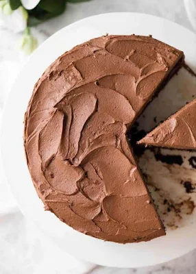 Chocolate Cake with Chocolate Buttercream Frosting on a white cake platter with a piece cut out, photographed from overhead