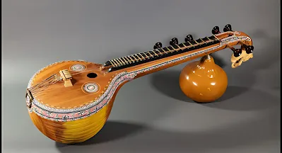 (b) Relate a string instrument with a wind instrument used in Carnatic music and write in detail.