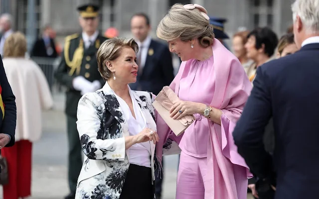 Duchess Maria Teresa wore a Chiaroscuro peak shoulder jacket by Alexander McQueen. Queen Mathilde wore a silk pink top by Natan