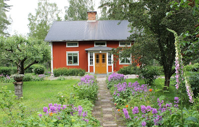 Huset är målat med falu rödfärg. Perennrabatter leder mot farstukvisten.