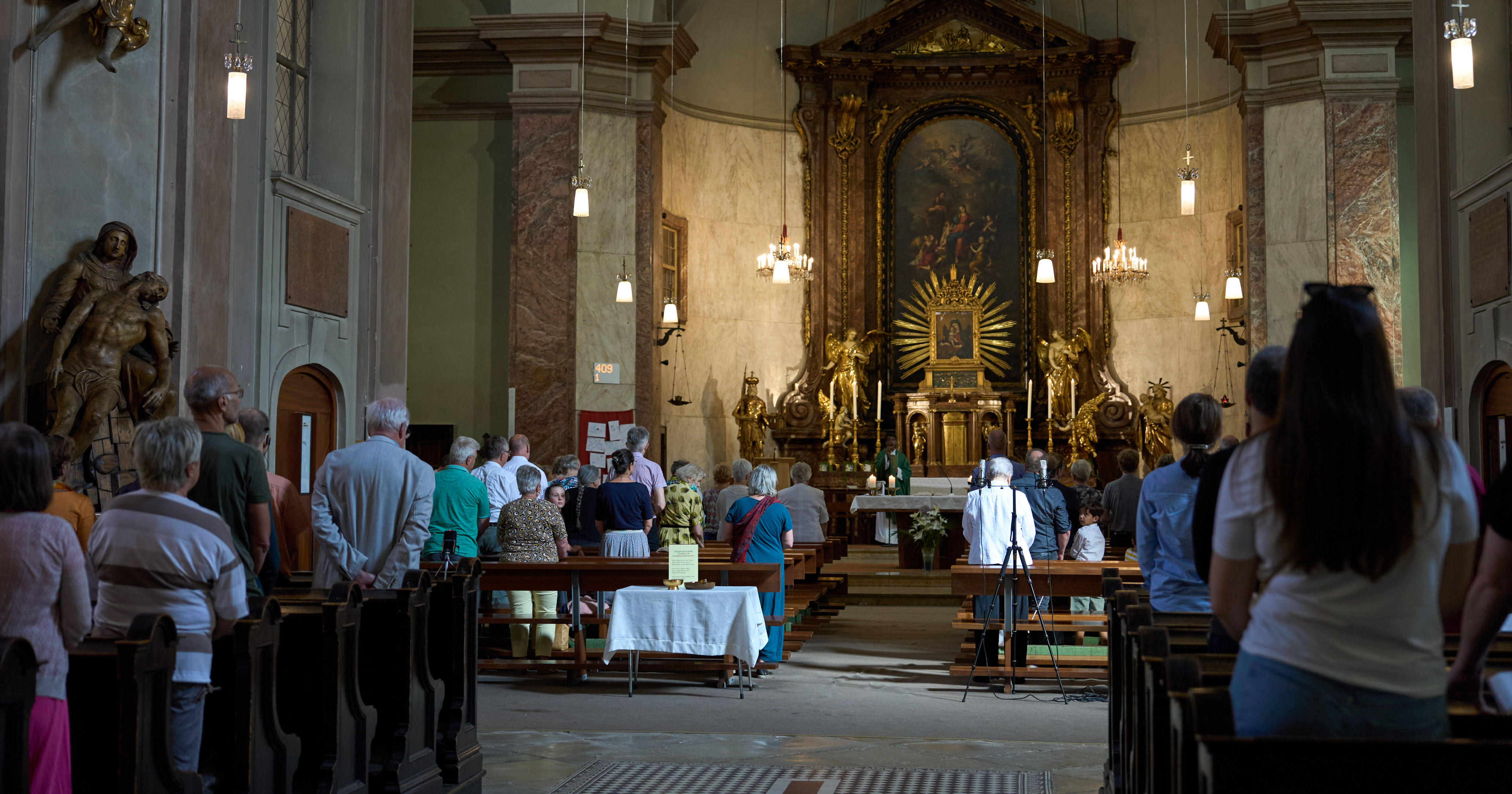 bei der Heiligen Messe von hinten nach vorne Richtung Altar - BesucherInnen beten stehend