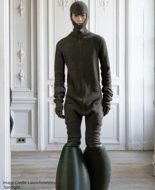 Photo of Rick Owens model at Paris Fashion Week. Model is wearing a full body onsie in dark frey with a balaclava attached to it. The model is also sporting rubber bubble-like shoes.