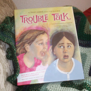 Photo of a book,Trouble Talk by Trudy Ludwig, illustrated by Mikela Prevost, on top of a folded, crocheted green zig-zag afghan