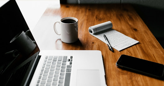 Notepad and pen, a coffee mug, a smartphone and a computer on eCommerce work table.