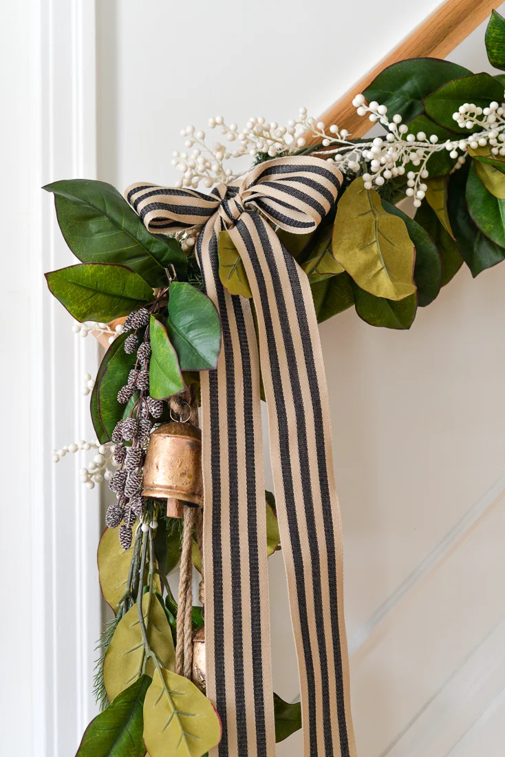 magnolia garland on stair bannister with brass bells and striped ribbon