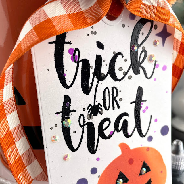 Trick or Treat tin tag created with: Scrapbook.com pumpkin patch layering stencil, slimline spiderweb stamp, halloween bats, nested tags die, pops of color in deep orchid and gloss black, solar white cardstock; Tim Holtz distress oxide in crackling campfire and villainous potion; Ranger super fine black embossing powder; Pinkfresh jewels