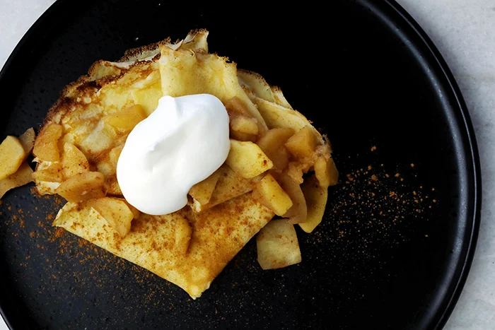 crepes with sauteed apples and whipped cream on a plate