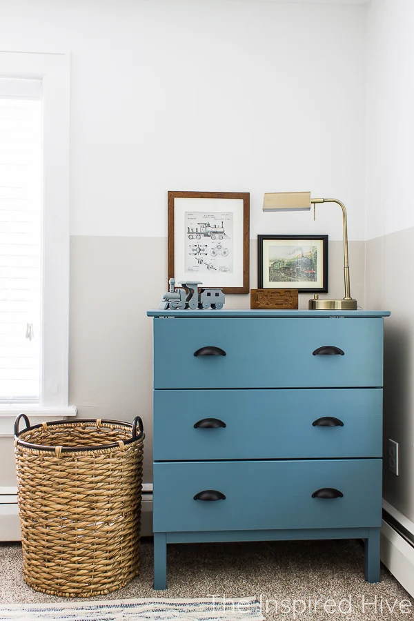 Blue dresser, brass lamp, and vintage train art