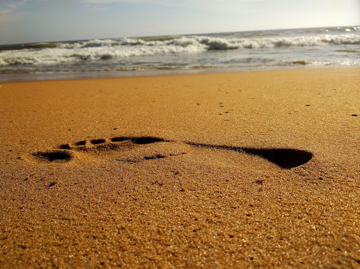 A footprint of a bare foot in the sand on a beach, with the sea in the background