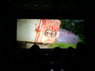 Haapsalu õudukafestival, hetk avatseremoonialt suures saalis. Ekraanil on suurelt mootorsaag ja selle peal verepritsmed.