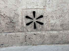 Six radially-oriented holes carved out of a piece of stone in a stone wall