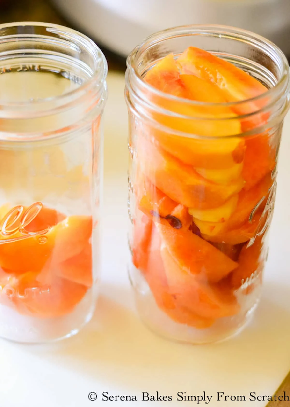 Two mason jars with sliced and peeled peaches in them for Whisky Peaches.