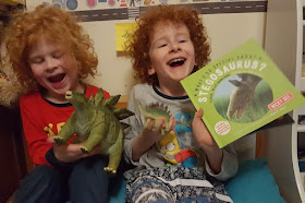 two boys holding stegosaurus book and plastic toy stegosaurus