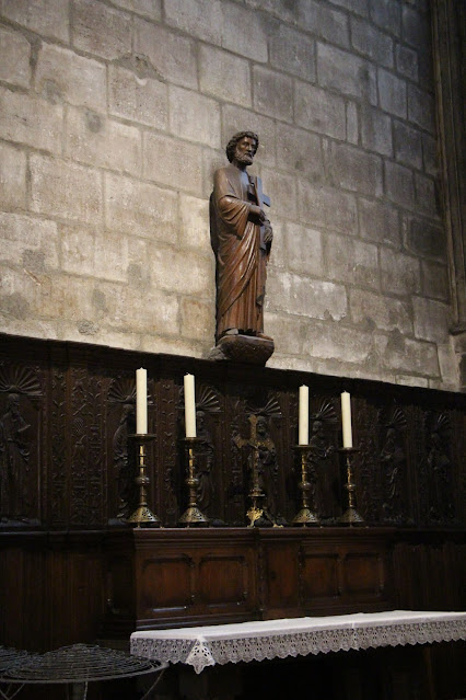 Side chapel at Notre Dame; wooden altar with white altarcloth and wooden wainscoting, stone walls, carved statue of a saint, candlesticks and candles, crucifix