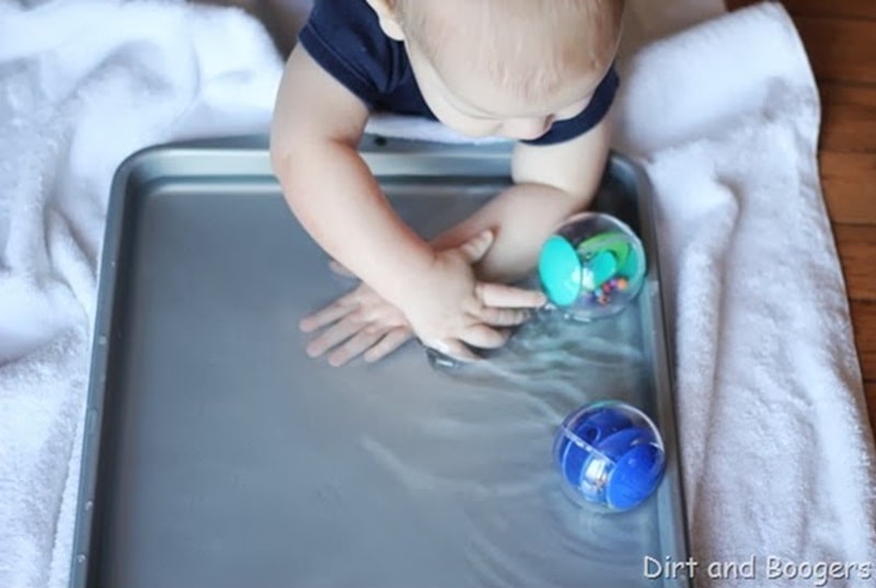 Baby playing with water and floating toys on a tray.