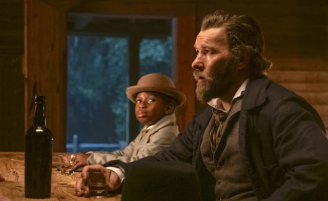 A Black boy and white man sit at a bar together