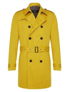 A bright mustard yellow trenchcoat done up with a thick yellow belt across the middle of it with big bold black buttons on a white background. 