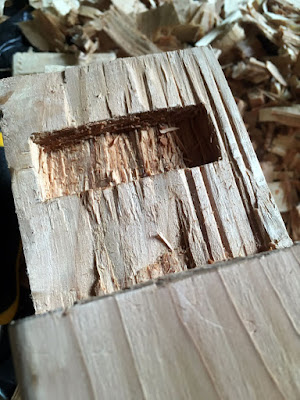 A photo from above showing the end of a beam and the tenon protruding from it, with the smaller rectangular mortise cute halfway through the tenon. The inset is very rough and looks crinkled, like pleated fabric.