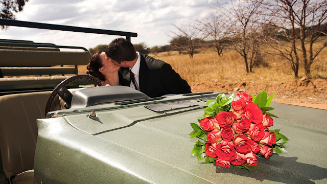 happy-bride-and-groom-kissing-while-driving-a-military-vehicle,-bouquet-of-flowers