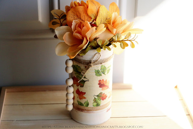 Faux floral displayed in a metal can that has been decorated with a napkin, twine, and wood beads