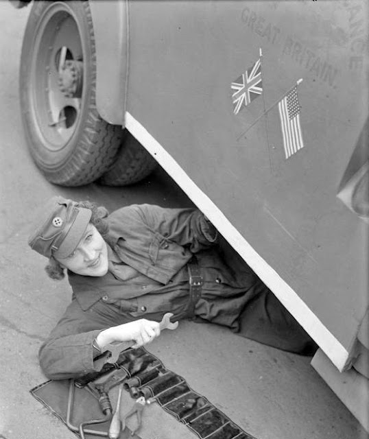 Women of the WW2 MTC - Mrs Pat Macleod slides out from under the ambulance she is repairing to smile for the camera. She is doing maintenance work on ambulance 8, which was presented by Elliott Nugent Esq. through the American Field Service.