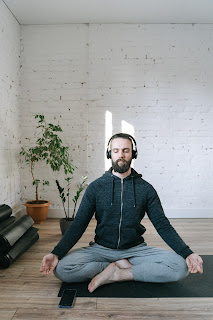 Man sitting on a cushion cross-legged while listening to music from a headset.