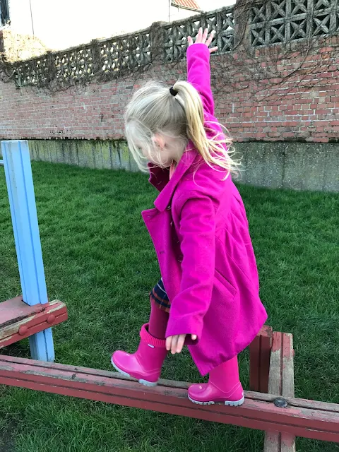 A 5 year old girl walking a long a thin piece of wood as part of an assault course with her arms out to balance her