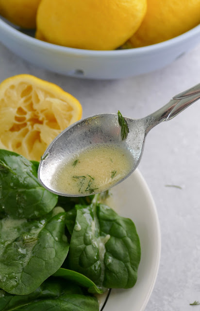 vinaigrette being poured from a spoon onto a spinach salad.