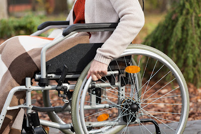 Pic of lady in wheelchair from waist down with focus on her hand on wheel and blanket on her lap