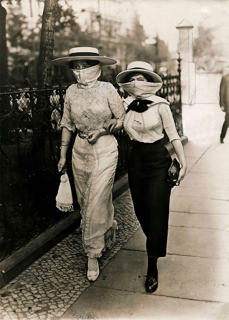 Black and white photograph of two elegant women walking arm in arm with masks during the Spanish flu epidemic