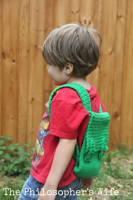 This is a side view of the little boy in a red shirt with a green backpack.  He is ready for an adventure! 