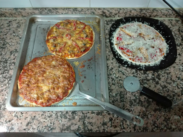 imagen de dos pizzas recién horneadas y una tercera a punto de entrar en el horno