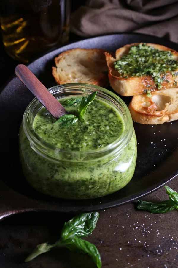 Easy Pesto Recipe in a Jar with Toasted Baguette Slices on a dark tray with a dark background