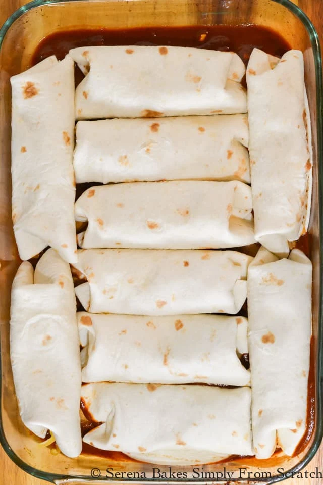 Filled Steak Burritos on top of homemade enchilada sauce in a glass pan.