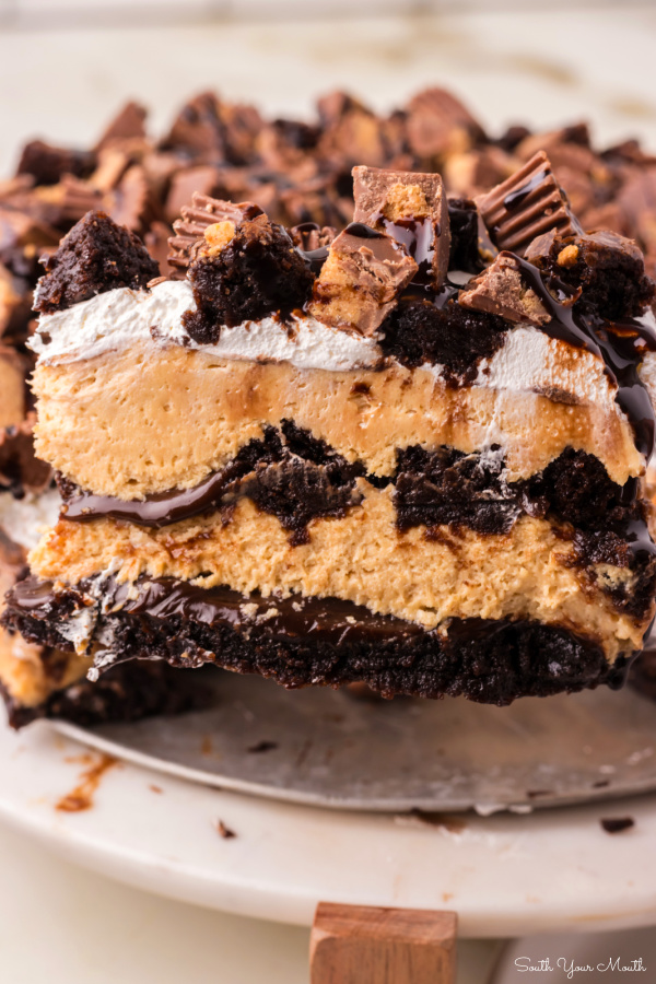 Peanut Butter Buckeye Brownie Cheesecake! An easy-to-assemble recipe with no-bake peanut butter cheesecake layered between brownie chunks and hot fudge sauce with peanut butter cups on top for a show-stopping buckeye dessert!