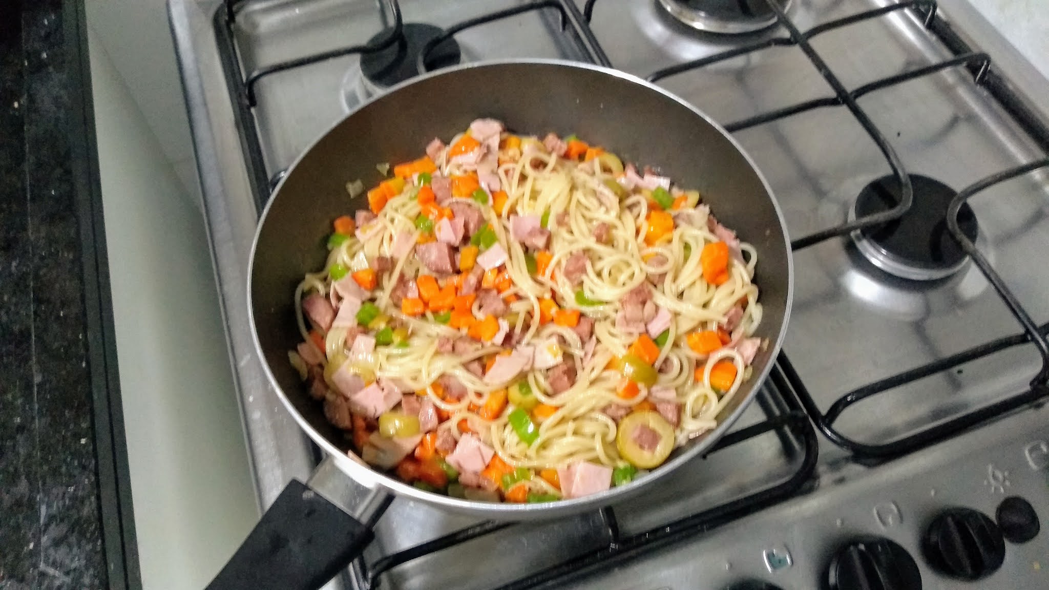 Espaguete com Linguiça Calabresa e Legumes dentro de frigideira alta em cima de boca de fogão