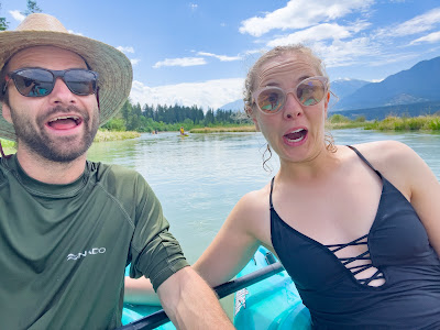 Image shows Lisa and Max making funny faces as they sit in kayaks on the Columbia River. You can see the high-water levels on the river in the background. Max's arm is holding onto the side of Lisa's kayak.