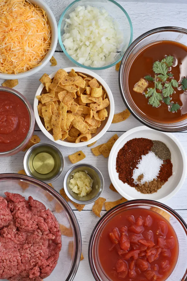 A collection of ingredients needed for Frito pie casserole on a white wood background.