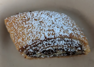 Piece of hazelnut/chocolate rugelach dusted with powdered sugar.