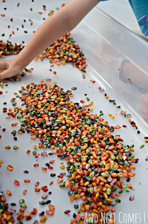 Playing with rainbow dyed puffed wheat cereal - a fun sensory play idea for toddlers & preschoolers from And Next Comes L