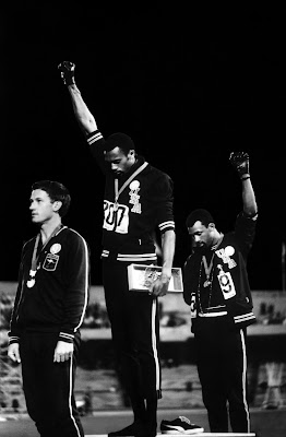 Olympic Athletes  Tommie Smith (center) and bronze medalist John Carlos (right) raise black-gloved fists during the American national anthem at the 1968 Olympics in Mexico City. Australian sprinter Peter Norman, who won silver in the 200 meters and supported Carlos and Smith's protest, stands at left