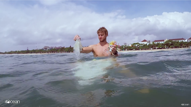 Alex Schulze on a surfboard picking plastic out of the water