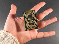 A hand holding a miniature, gold stamped book.