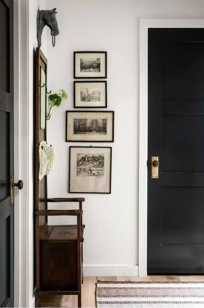 Vintage photographs hung vertically on white wall next to black door in entryway