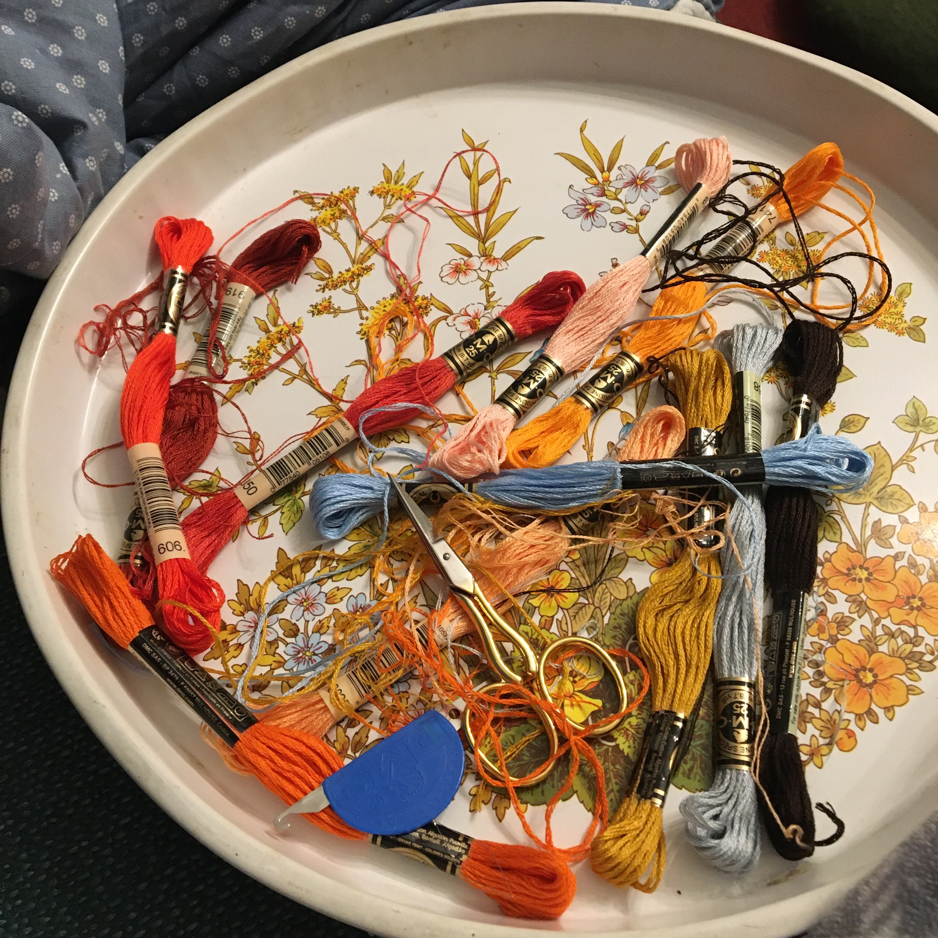 A circular tray with a colorful floral design containing different colors of embroidery floss.