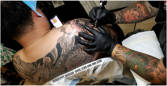 man sitting getting a black and grey dragon with peonies flowers at Horipeppe  Mukade's tattoo artist tattoo shop in Sacramento California