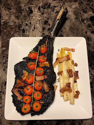 Cowboy ribeye grilled Pittsburgh rare, with blistered cherry tomatoes and grilled white asparagus with bacon