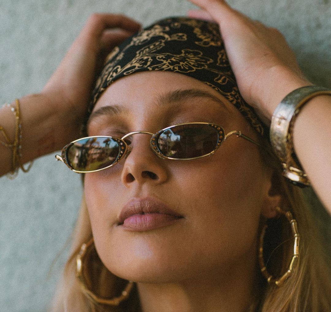 Woman with blond hair wearing large gold hoop earrings, 90s oval sunglasses, and bandana