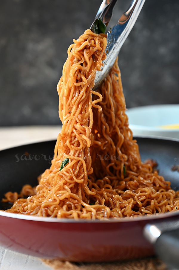 sesame garlic ramen noodles  lifted by a pair of tongs