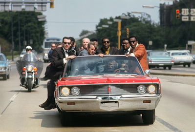 photo of Robert Kennedy with aides including former prizefighter Tony Zale and (right of Kennedy) NFL stars Lamar Lundy, Rosey Grier, and Deacon Jones in red convertible, 1968